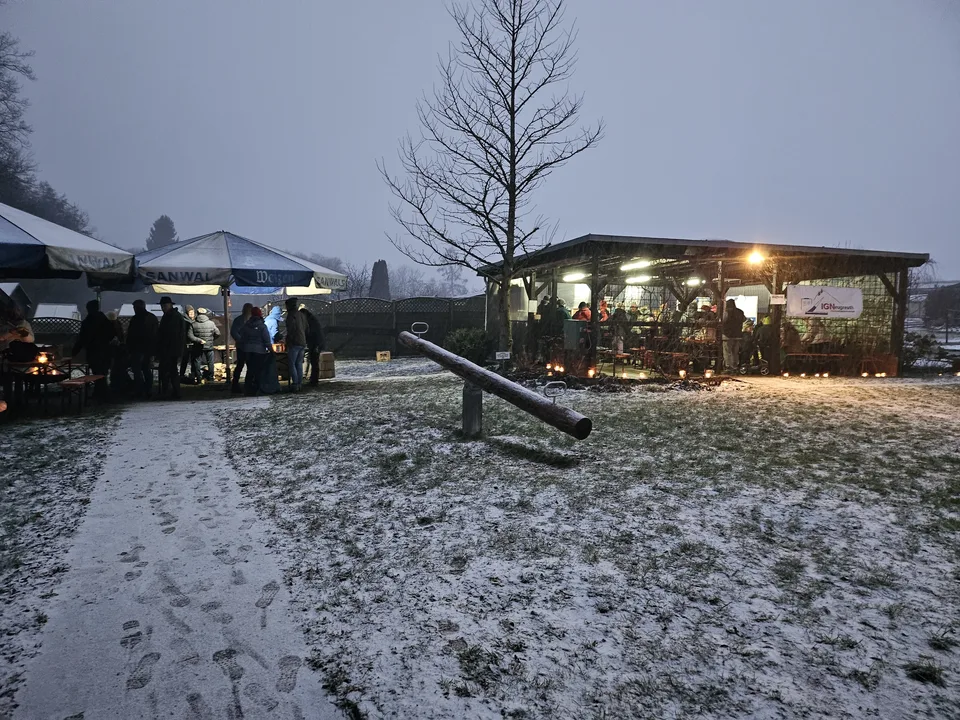 Wintergrillen am Abend: verschneites Gelände mit beleuchtetem Pavillon und Schirmen
